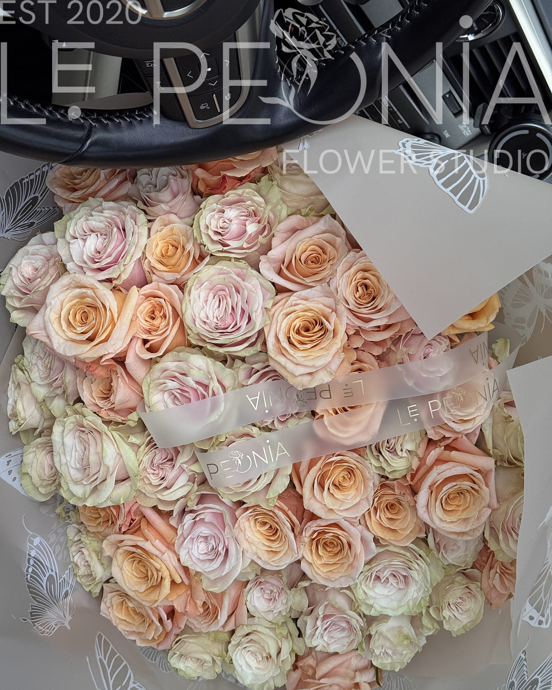 Large round bouquet of pastel garden roses in soft blush, peach and ivory shades, wrapped in transparent butterfly-patterned paper
